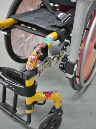 Zippy Zone with two Oval Bridge clamps, spanned by an Adapter Plate 2. The L-Angle Extension positions Wheelchair Bracket and post to allow brake actuation.